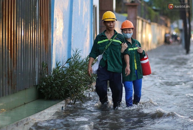 Hai vợ chồng công nhân tay trong tay lội qua đoạn đường ngập. Ảnh: Khang Thái.