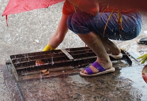 Người phụ nữ thông cống thoát nước trong cơn mưa chiều 19/2 trên đường Song Hành (Quận 12, TPHCM)