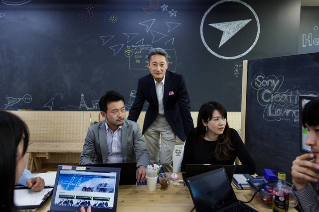 Ông Kazuo Hirai (mặc áo vest đen) cùng nhân viên trong căn phòng mang dáng dấp startup Mỹ.
