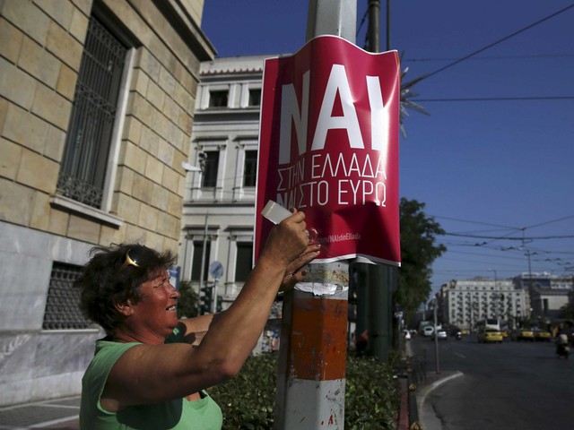 woman puts up a referendum campaign poster in greece