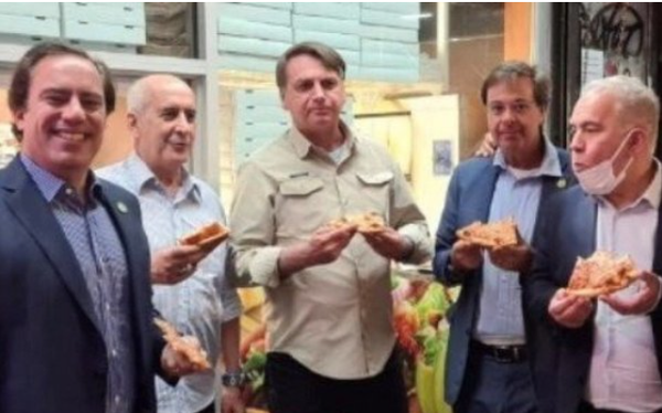 Tổng thống Brazil (ở giữa) phải đứng ăn pizza ở ngoài đường tại New York, Mỹ vì chưa tiêm phòng vắc-xin Covid-19. (Ảnh: Reuters)