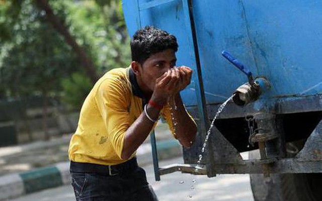 Một người lao động uống nước từ một chiếc xe bồn tại công trường xây dựng.