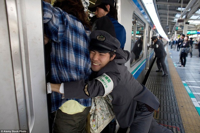 Nhân viên sân ga đẩy hành khách vào trong những toa tàu chật cứng ở Nhật Bản. Ảnh: Alamy